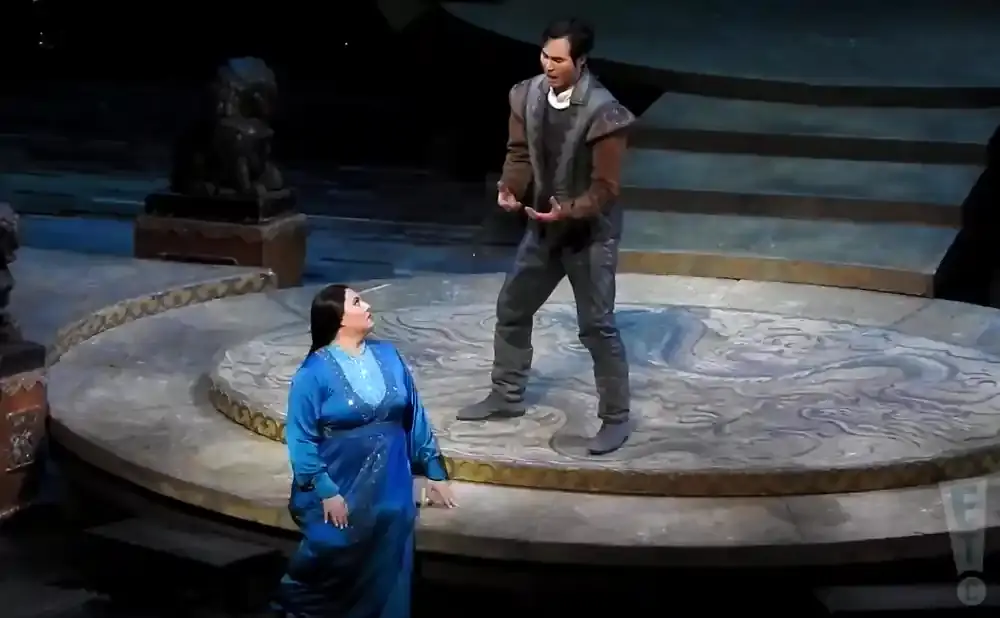 Opera singers in costume on a circular stage with blue and gray designs.