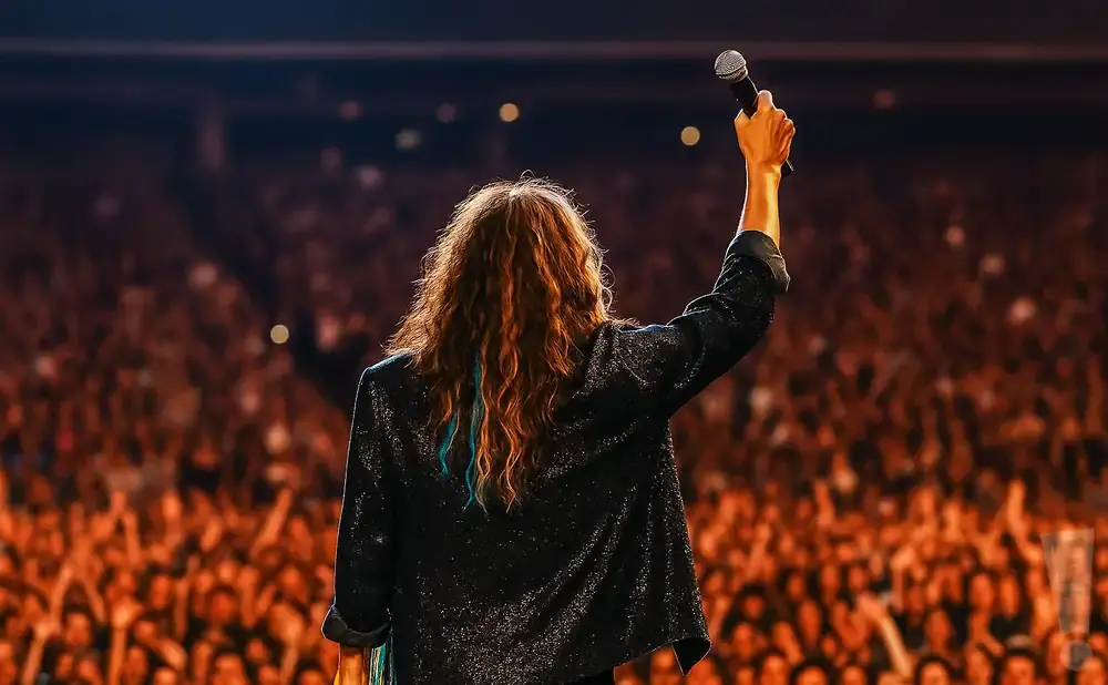 A singer holds a microphone aloft to a cheering crowd.