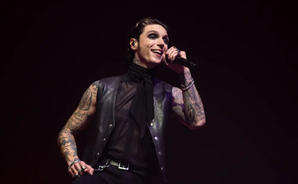 A tattooed man with heavy eye makeup sings into a microphone.