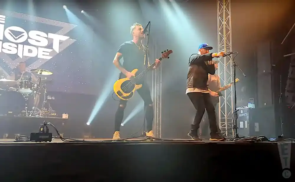 Band members performing on stage, one playing a yellow bass guitar, another singing into a microphone.