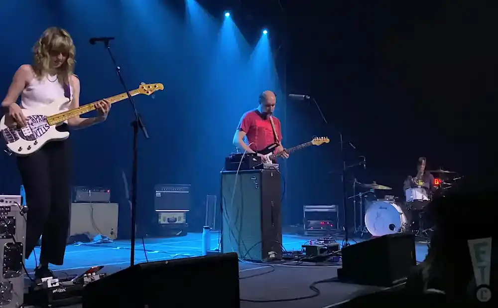 A band plays on a stage with blue spotlights. The bassist is in the foreground.