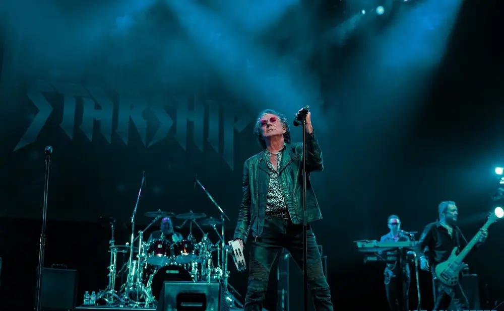 Mickey Thomas of Starship performs on stage in a leather jacket.