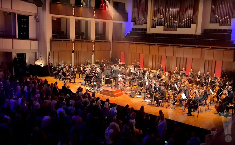 An orchestra performs for a live audience in a concert hall.