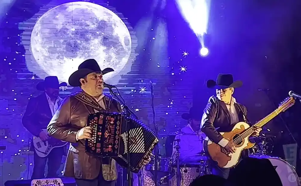 A mariachi band performs on stage under a giant moon projection.