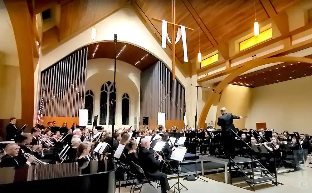An orchestra in a church, with a conductor leading them and an organ in the background.