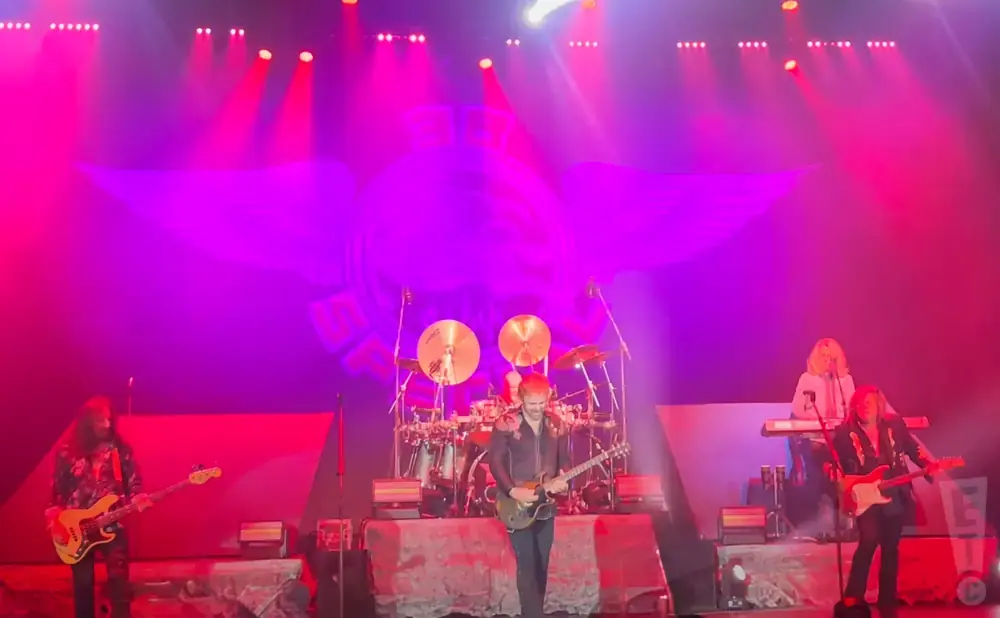 A band performs on stage under purple and pink lights.