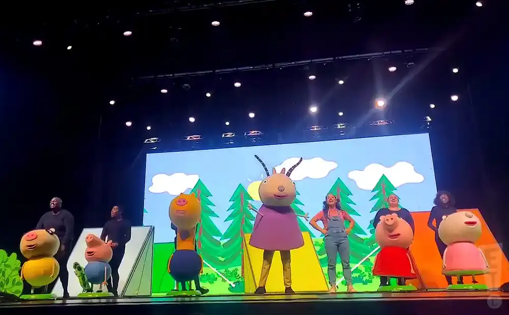 Peppa Pig characters and costumed performers on a stage with a cartoon backdrop.