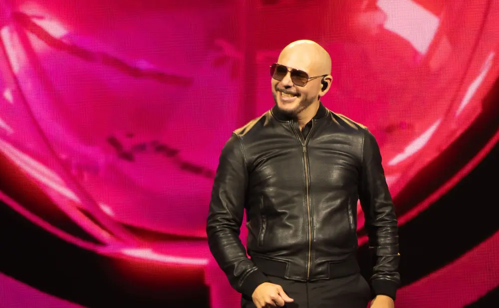 Pitbull wearing sunglasses and a black leather jacket smiles on a pink stage background.