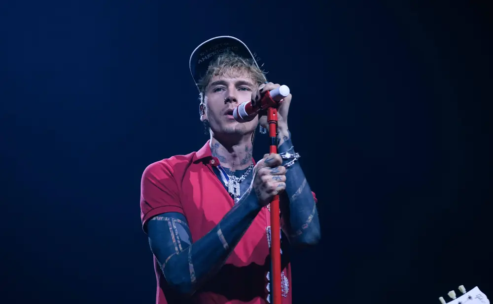 Machine Gun Kelly performs in a red polo shirt, black cap, and large diamond chain.