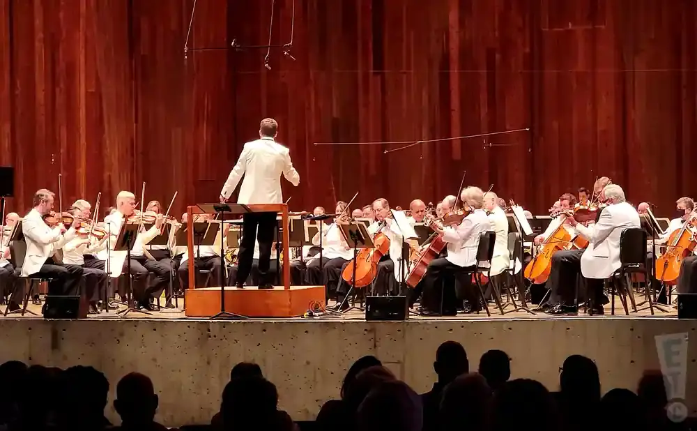 Orchestra in white jackets performs on stage with a conductor.
