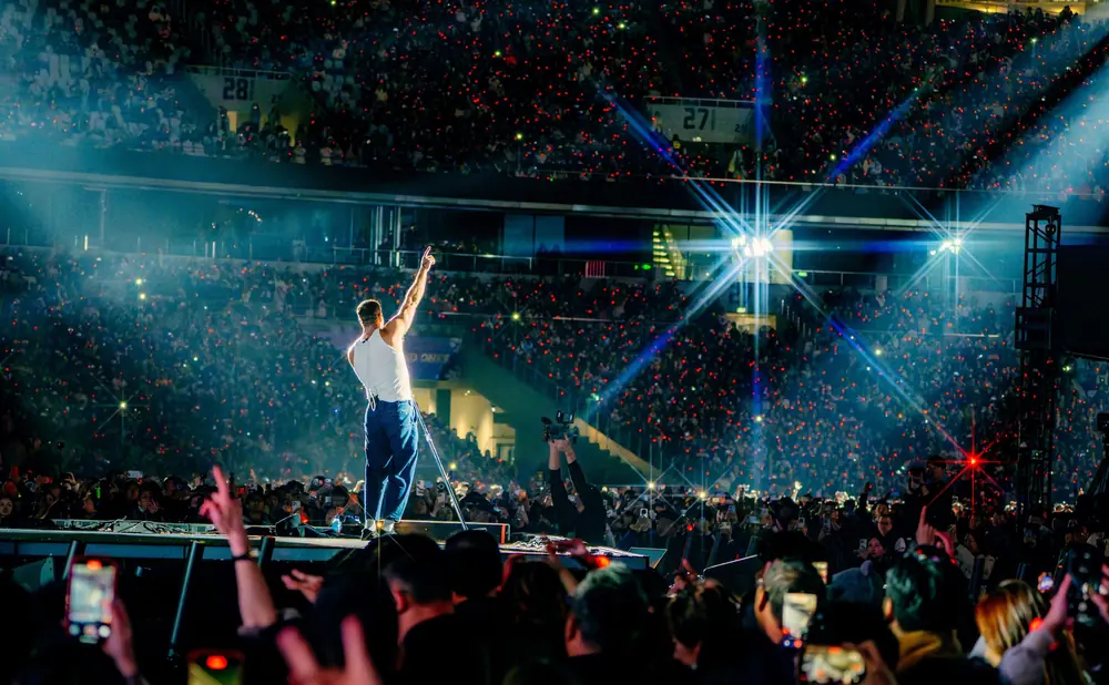 Singer performs on stage with a stadium crowd holding up red lights.
