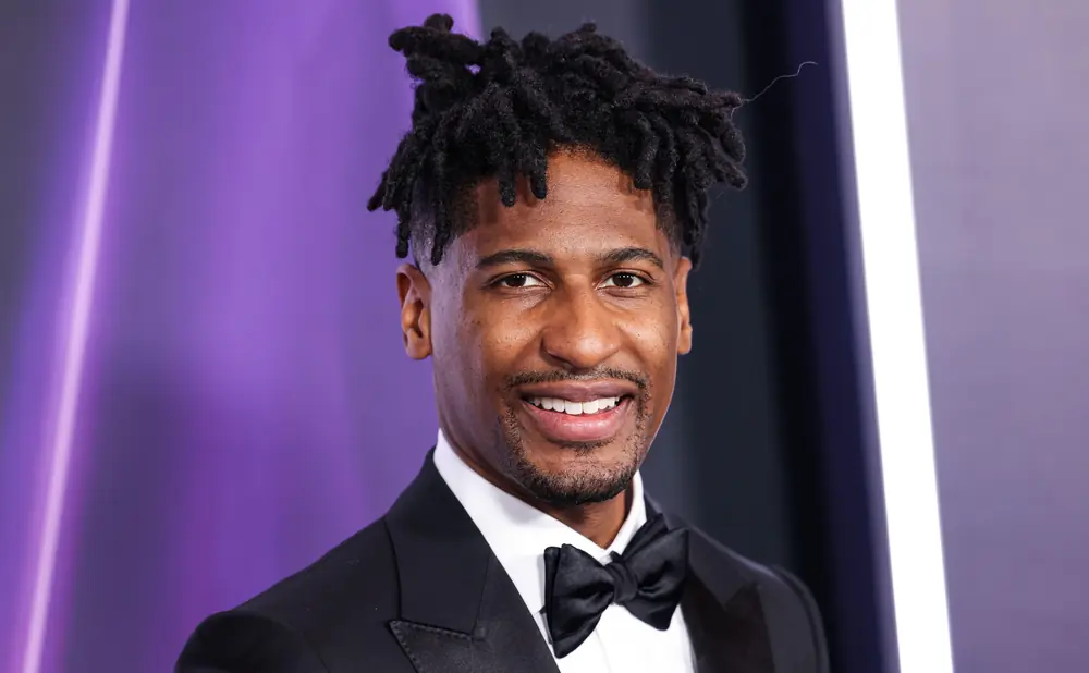 A man with dreadlocks in a tuxedo and bowtie smiles.