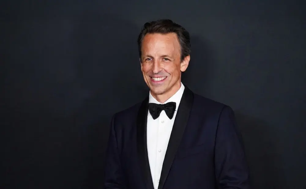 A man in a tuxedo smiles against a dark background.