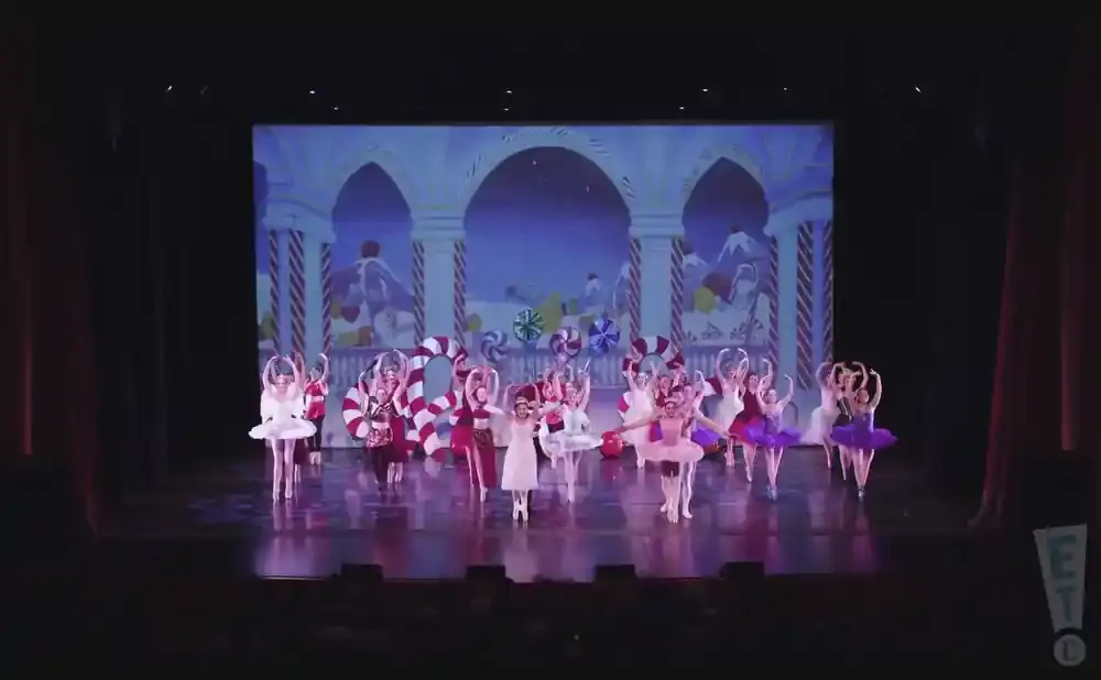 Dancers in tutus perform a ballet on stage with a candy-themed backdrop.