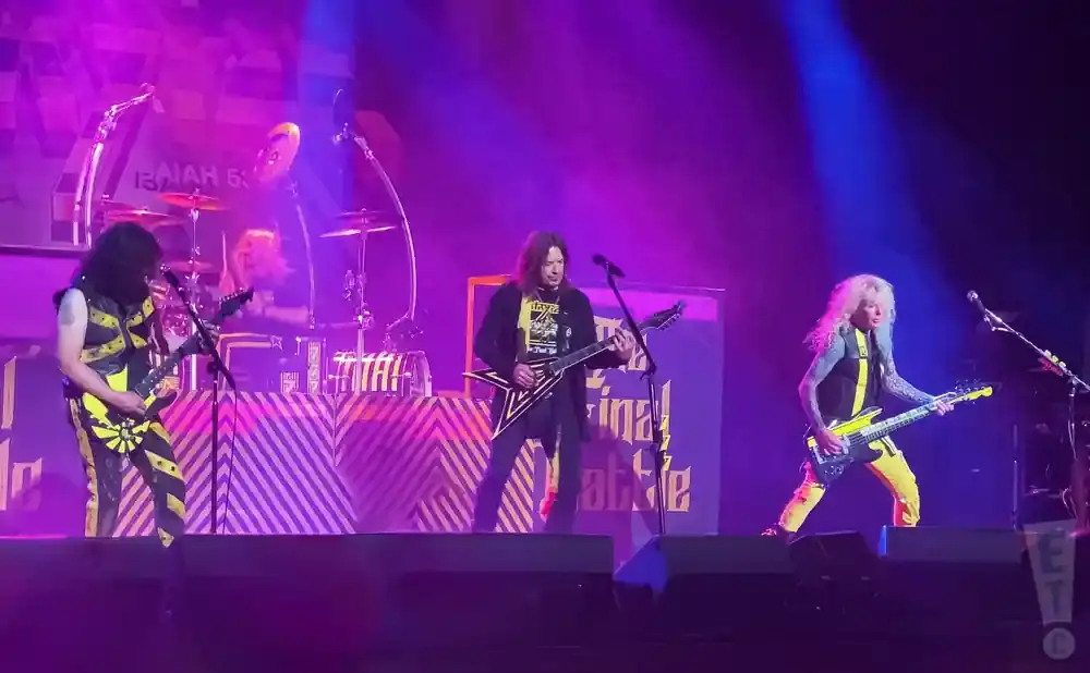 A heavy metal band performs on stage with bright purple and blue lights.