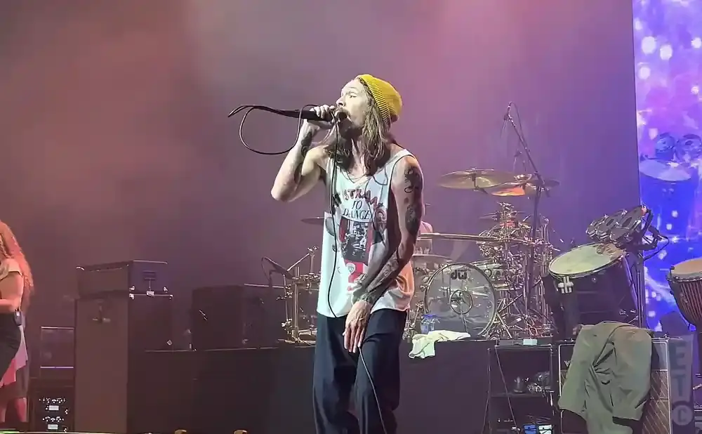 A male singer with a yellow beanie sings into a microphone on stage.