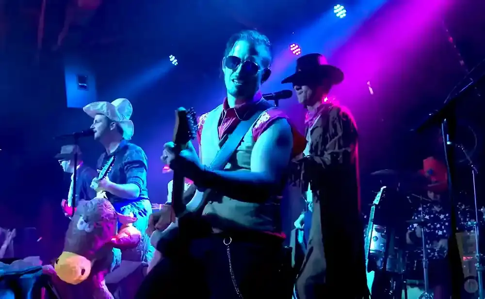 Band members in cowboy hats perform on stage, one playing guitar and another at the drums.