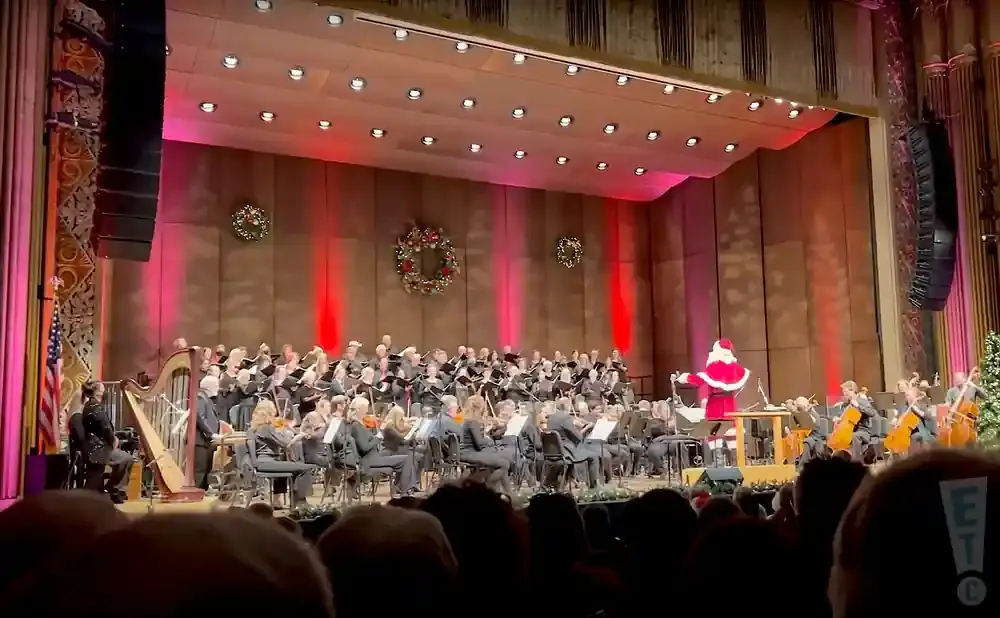 Santa conducts an orchestra and choir during a holiday performance.