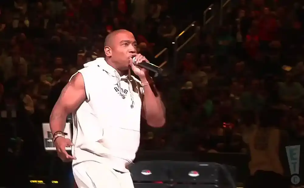 Rapper Ja Rule performs on stage at a concert, wearing a white sleeveless hoodie and pants.