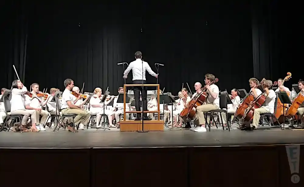An orchestra performs on stage, led by a conductor.