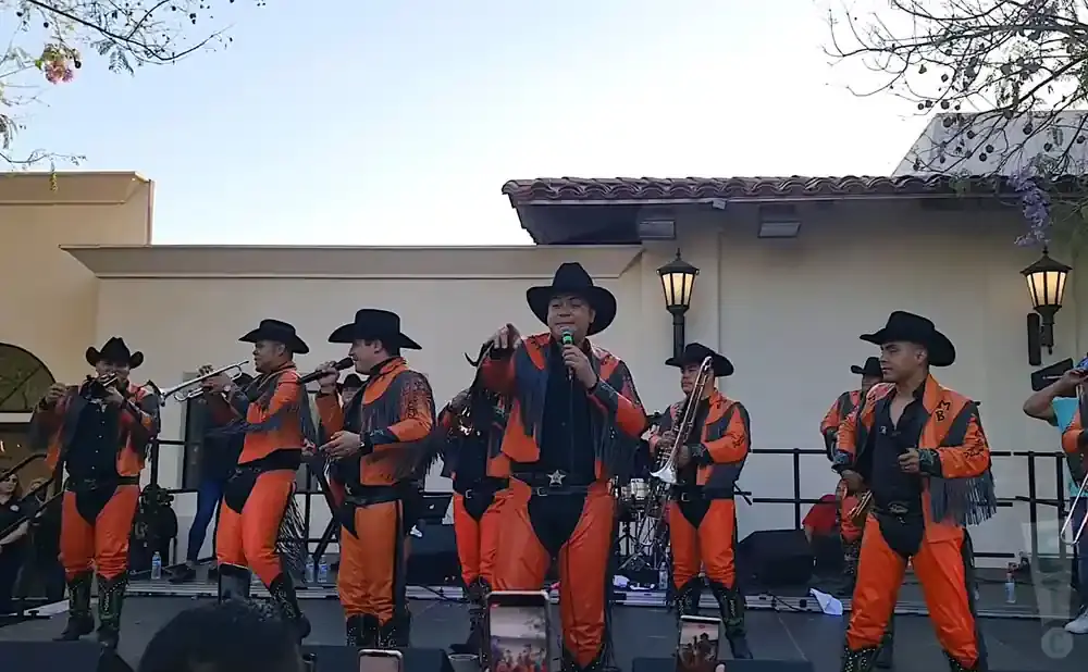 A band in orange and black outfits performs on stage, wearing cowboy hats.