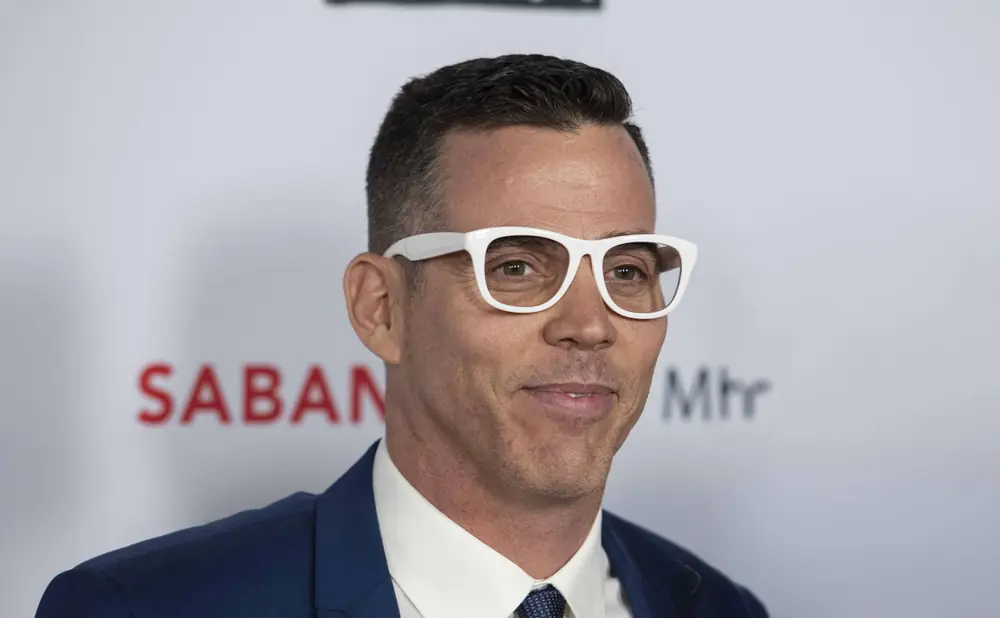 Steve-O wearing white-rimmed glasses and a blue suit.