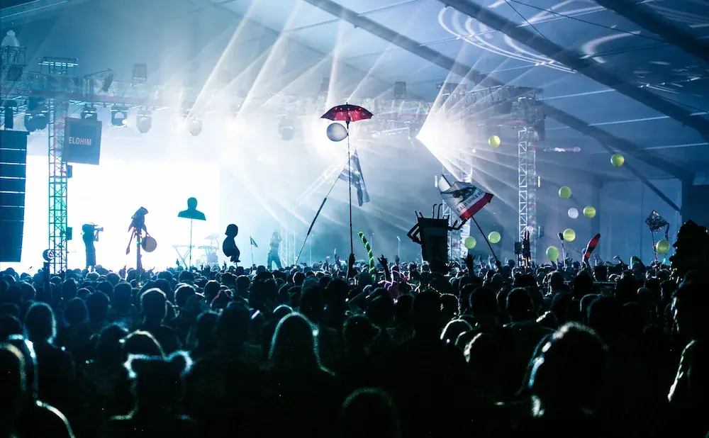 A silhouette crowd at a concert with bright stage lights and balloons.