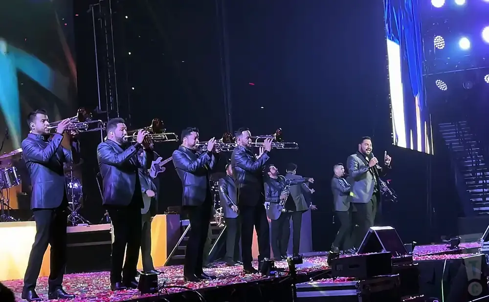 A mariachi band performs on stage in sparkly jackets, with a lead singer addressing the audience.