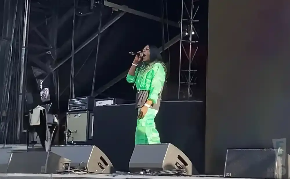 Rapper Lil Mama performs on stage in a bright green outfit.