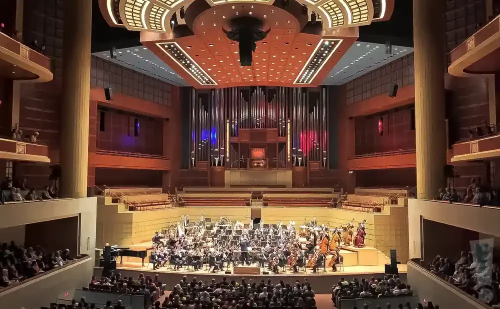An orchestra performs on stage in a grand concert hall with a large pipe organ in the background.