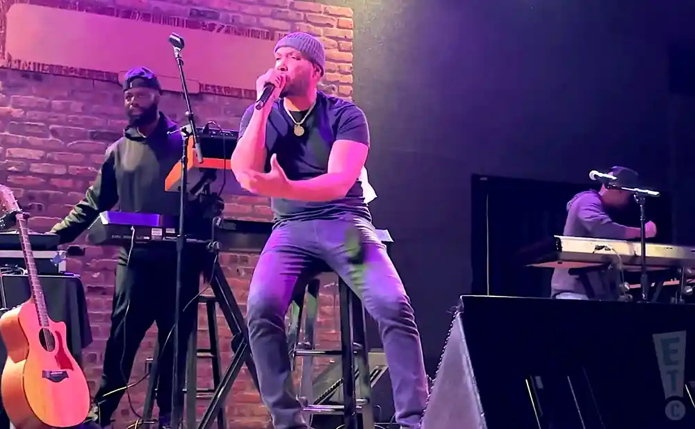 A singer performs on stage with a keyboard player and a guitarist.