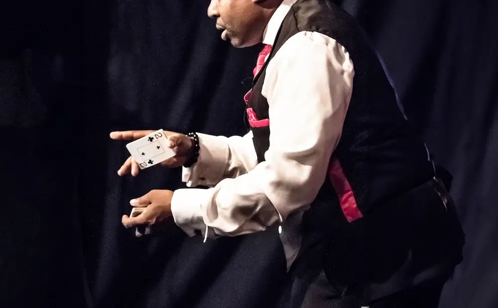 Magician's hands in motion, one holding a playing card, the other cupping a deck.