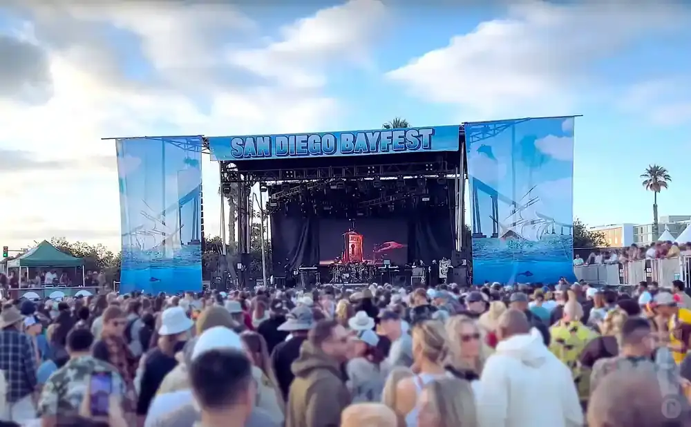 Crowd at San Diego Bayfest with a stage and banners featuring ships and bridges.