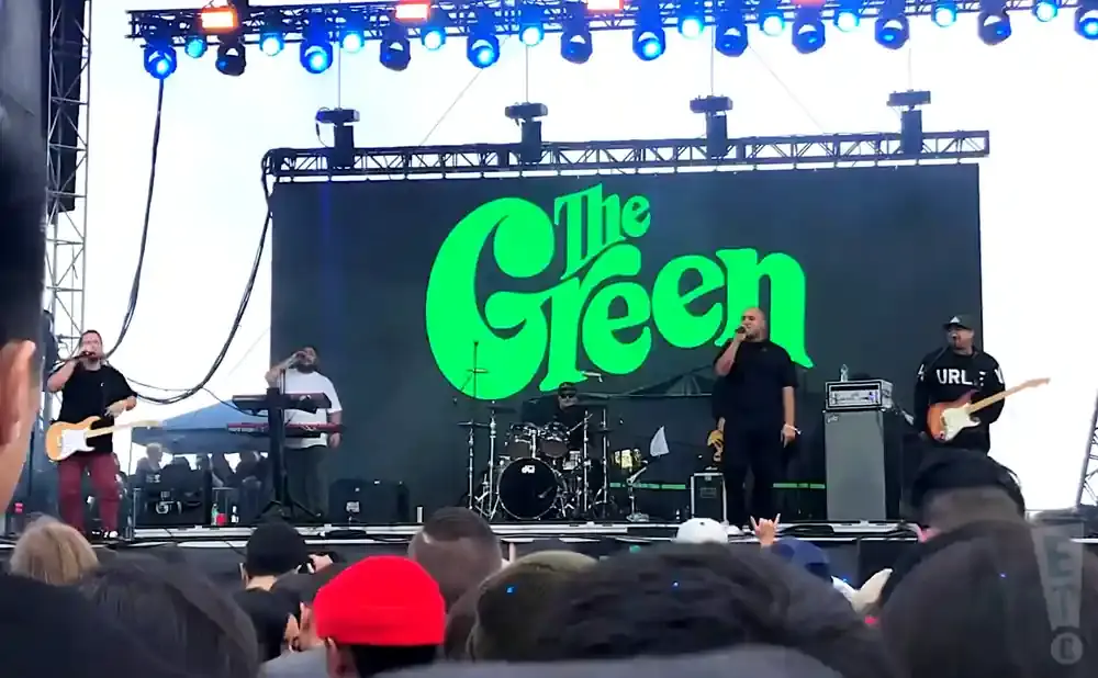 The Green band performing live on stage with a large green logo displayed behind them.