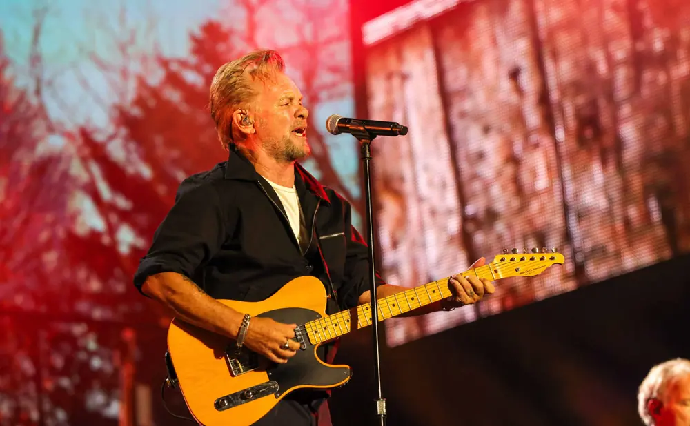 Bruce Springsteen sings and plays a yellow guitar on stage with a blurry red backdrop.