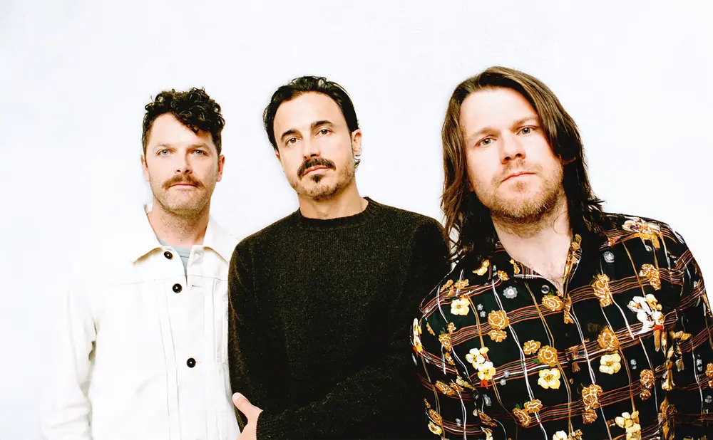 Three men in dark clothing pose against a white background.