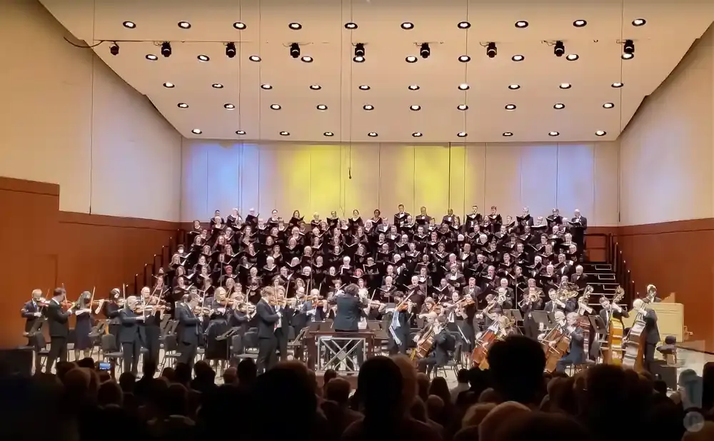 An orchestra and choir perform on a brightly lit stage.