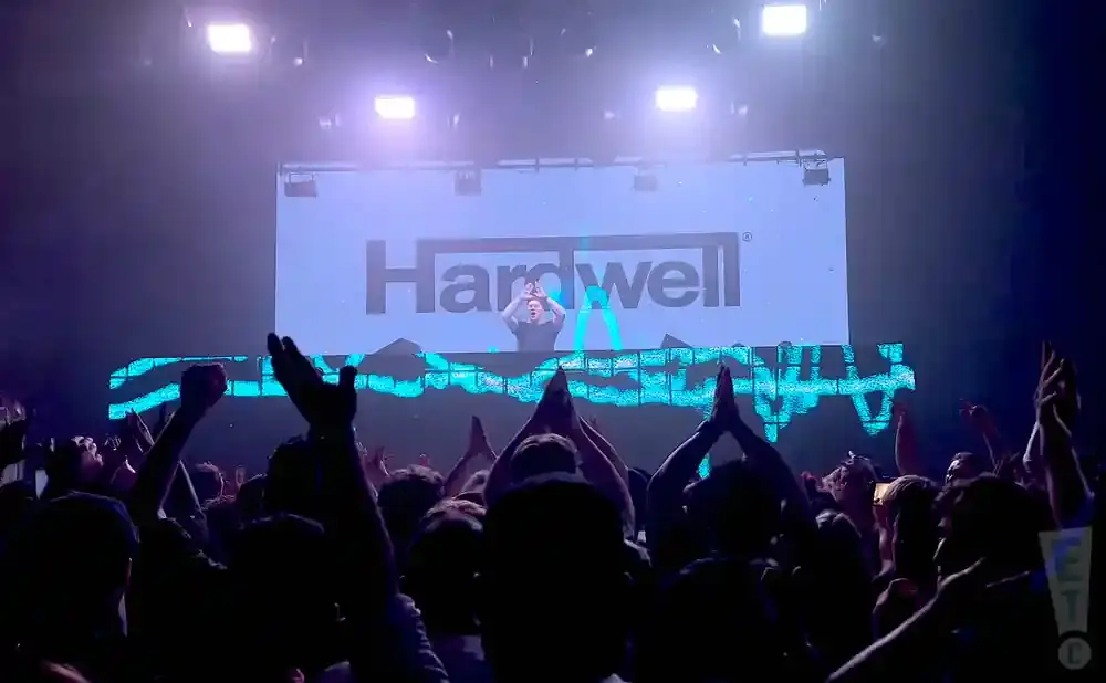 DJ Hardwell performs for a cheering crowd at a concert with his name displayed on a large screen.