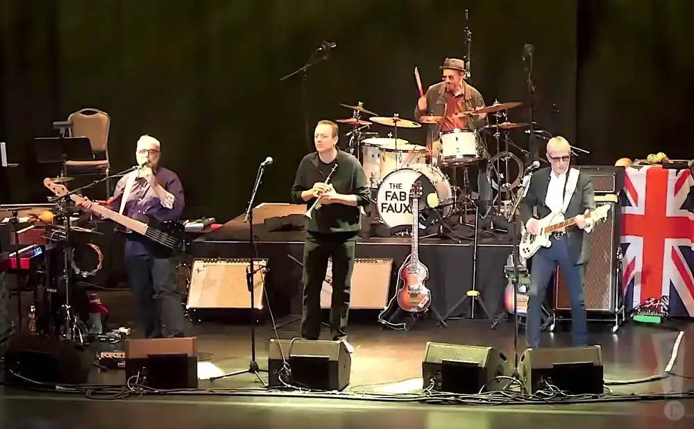 A band plays on stage, with a bassist, trumpeter, guitarist, and drummer visible.