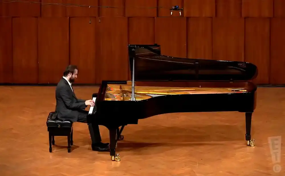 Pianist in a suit plays a grand piano on stage.