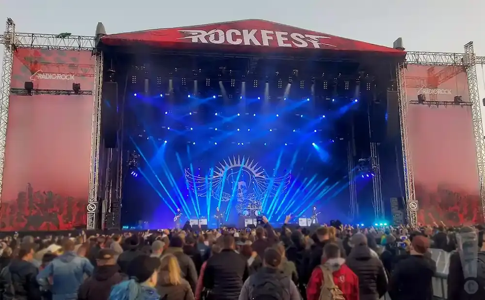 A large outdoor concert stage at Rockfest, illuminated by blue lights, with a crowd in the foreground.