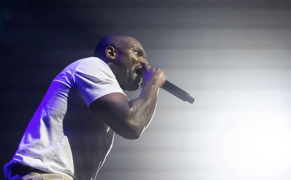 A Black man in a white t-shirt sweats as he raps into a microphone on stage.