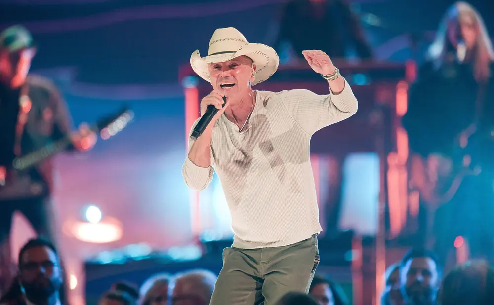 A man in a cowboy hat sings into a microphone on stage.