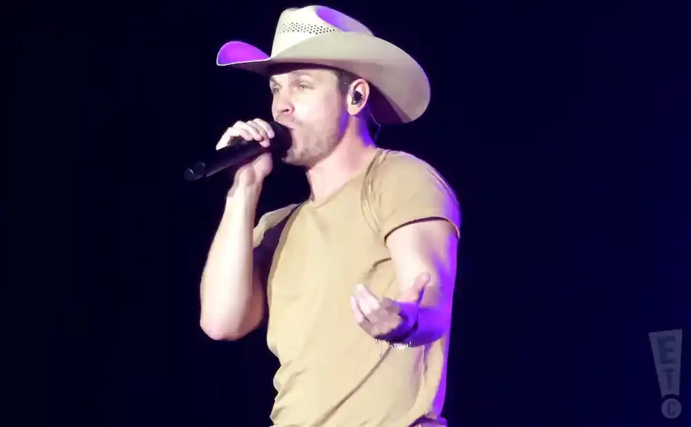 A male country singer in a cowboy hat performs on stage, holding a microphone.