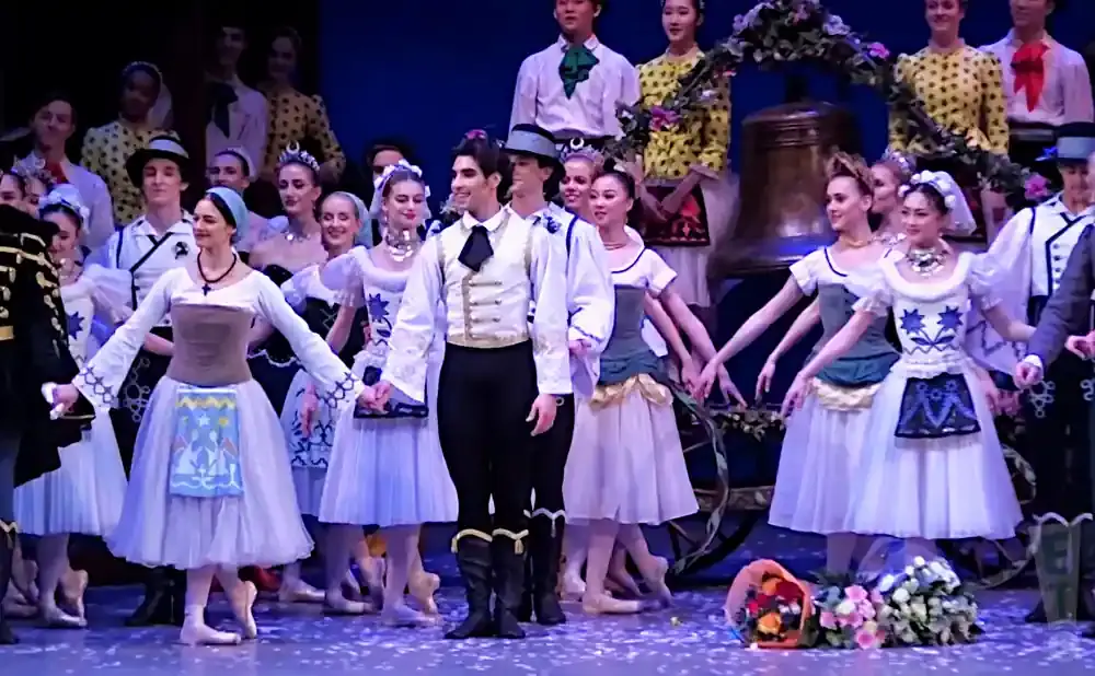 Ballet dancers in colorful costumes perform on stage with bouquets of flowers.