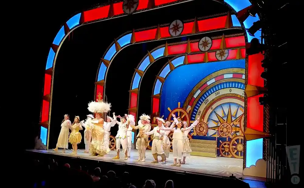Stage performers in nautical costumes on a set with a large compass rose.