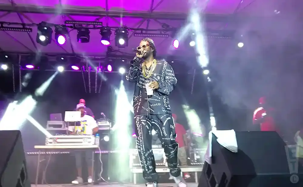 A rapper in a patterned suit performs on a smoky stage under purple lights.