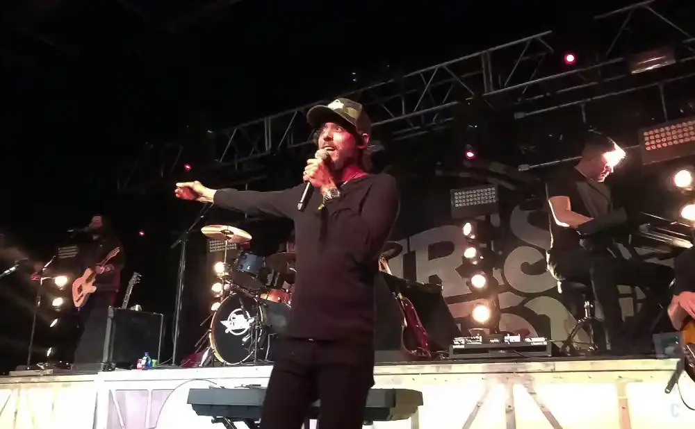 A band performs on stage, with the lead singer holding a microphone and a guitarist in the background.