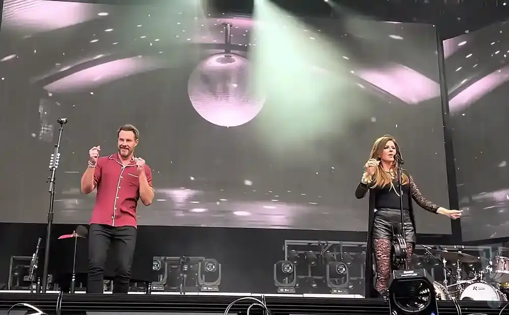 Shania Twain and an unidentified man perform on stage, with a disco ball above them and screens displaying a starry background.