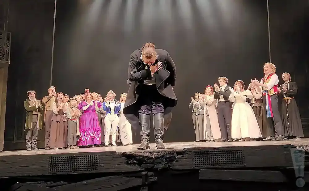 A group of performers in costume bow to an audience from a stage.